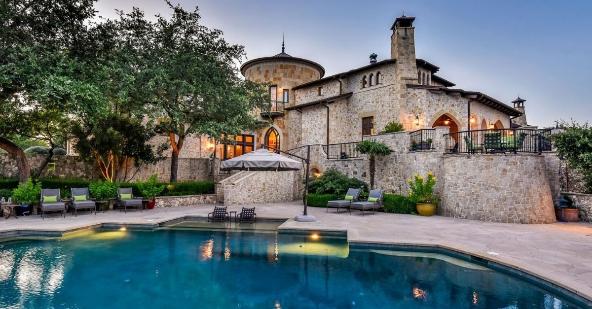 Castle looking house with light stone walls and sparkling blue pool