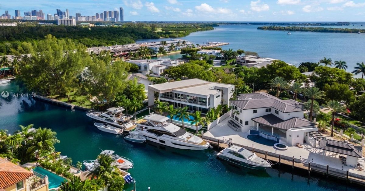 Very large modern white house with multiple yachts parked on its dock in Miami