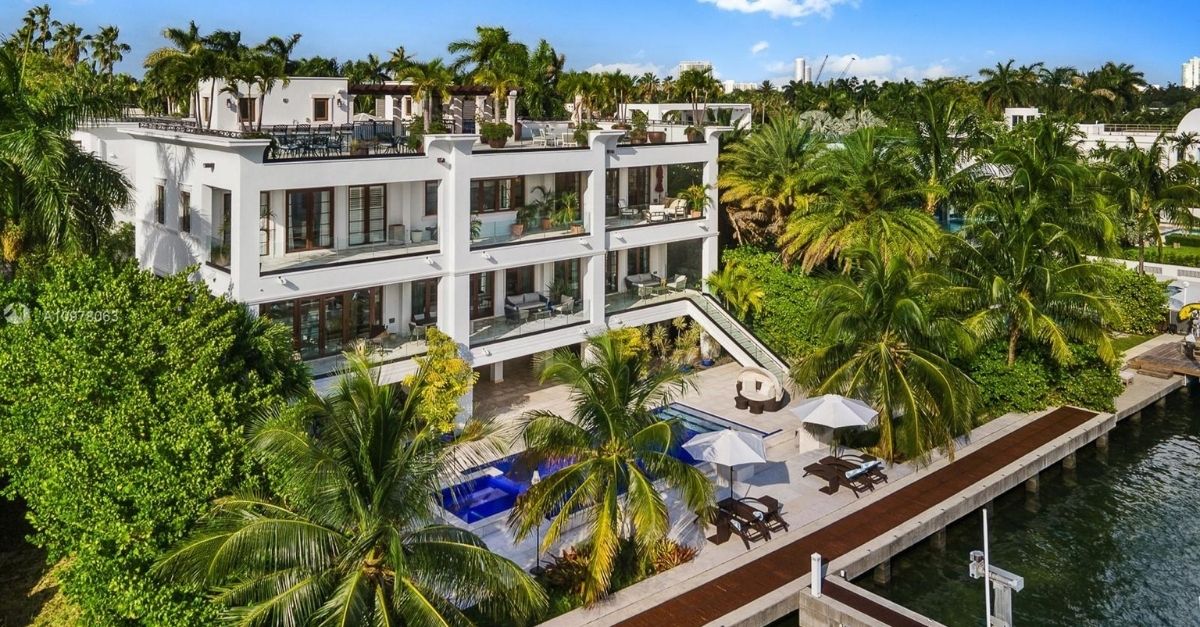 Oversized, modern white house on Miami waterfront with swimming pool and lots of lush and tropical trees outside