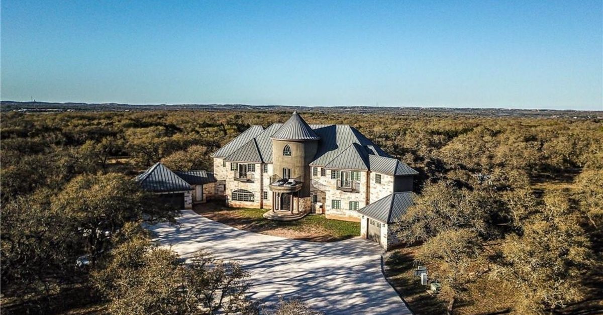 Castle-like home surrounded by mature oak trees with metal roof and light stone work