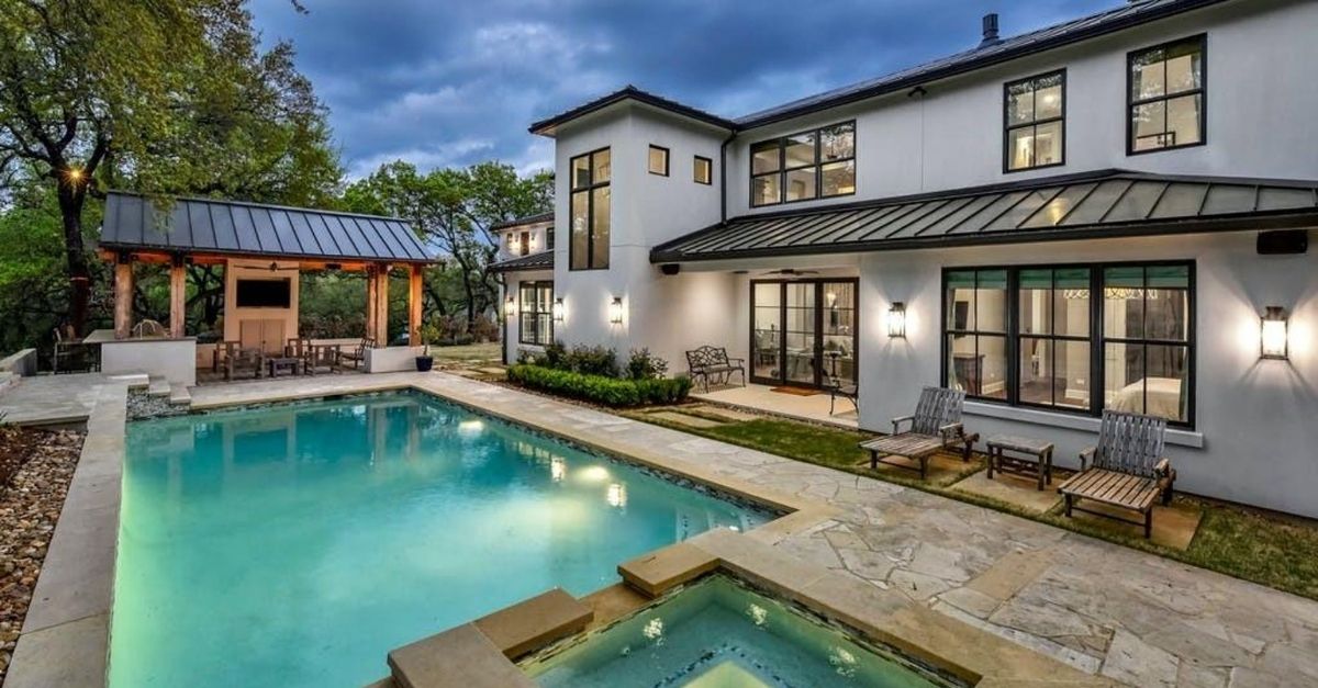 Contemporary style home with metal roofs and large windows behind a sparkling pool of a home for sale in Austin